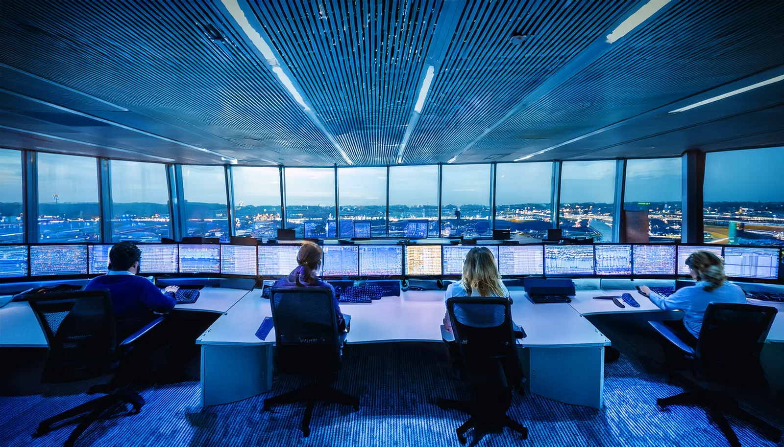 Personnel dans une salle de contrôle des opérations d’un aéroport, vu de dos, devant de grands écrans