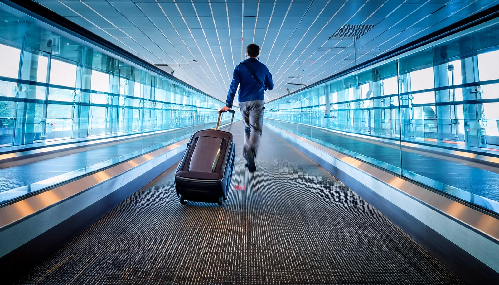 Voyageur avec une valise qui se hâte dans un long couloir de correspondance d’un aéroport