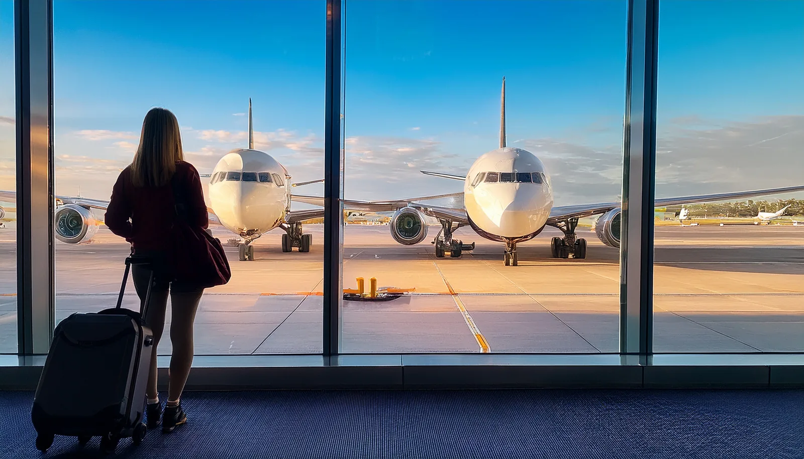 Voyageur avec une valise regardant par une fenêtre du terminal deux avions, chacun à sa porte d’embarquement