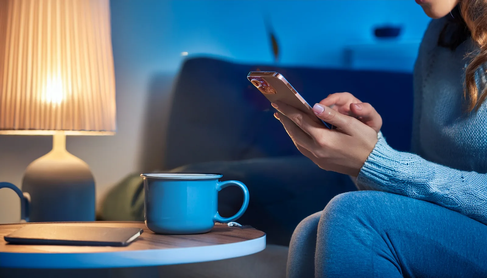 Voyageur sur un canapé le soir, regardant son téléphone portable, avec une tasse à côté