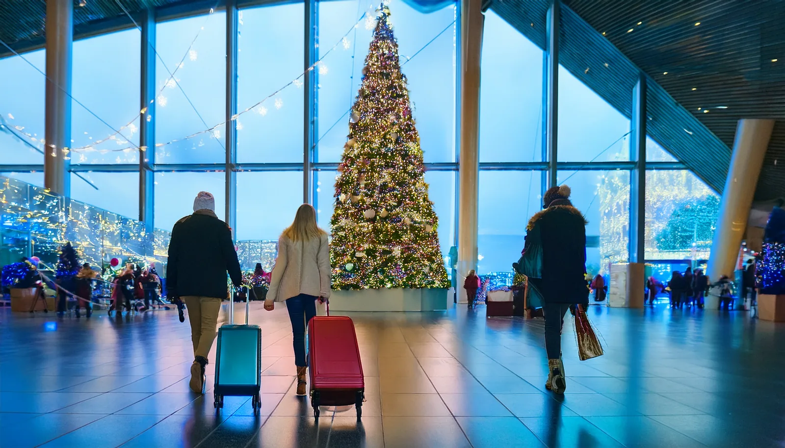 Voyageurs avec des valises dans un terminal d’aéroport décoré pour Noël avec un grand sapin, vus de dos